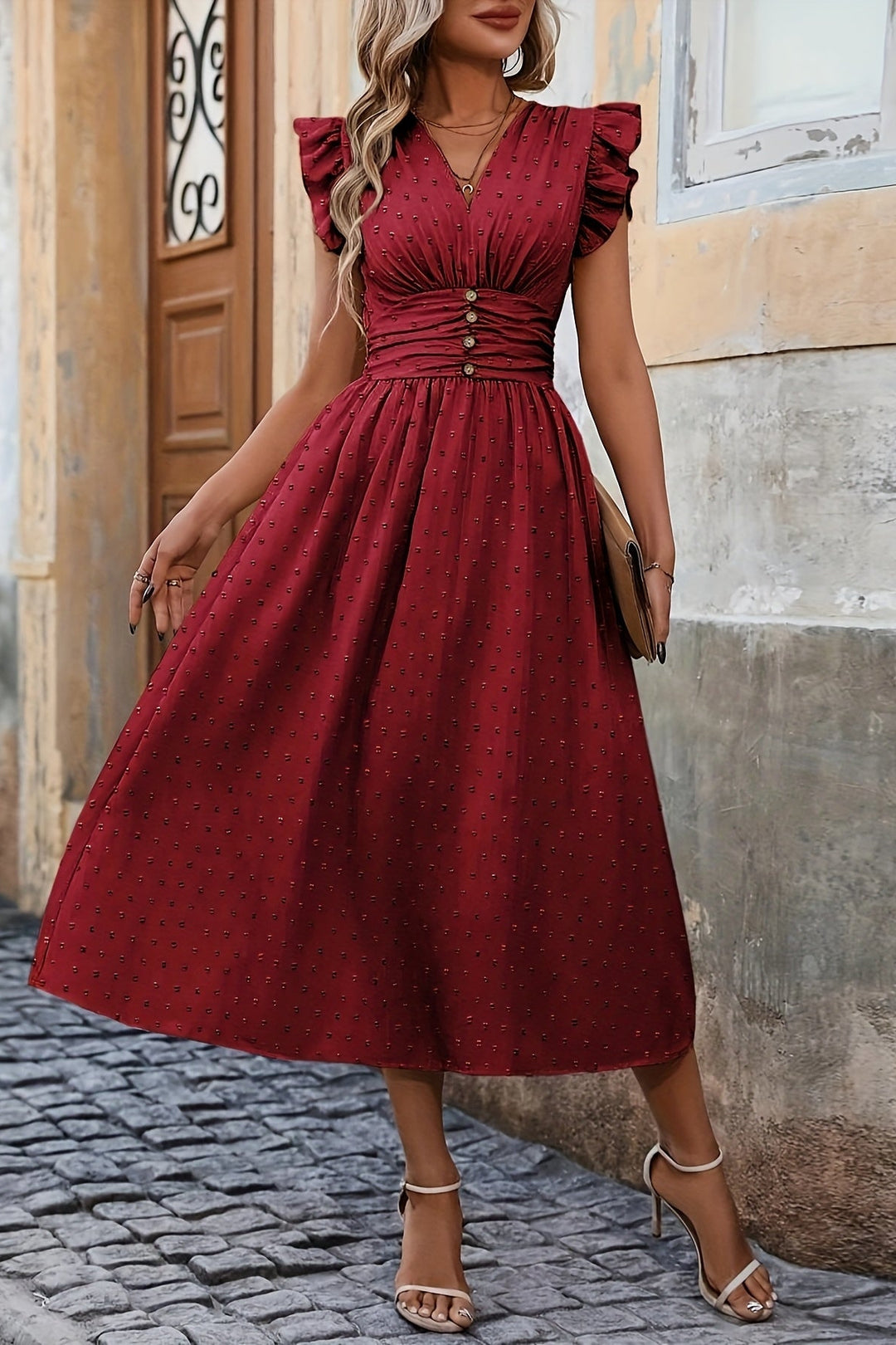 Woman wearing a red dress standing on a cobblestone street.