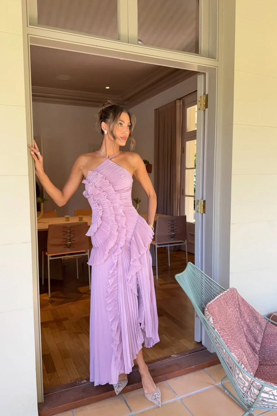 Woman in a lavender one-shoulder dress standing in a doorway.