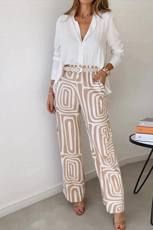 Woman wearing a white blouse and patterned beige pants standing in a minimalistic room.