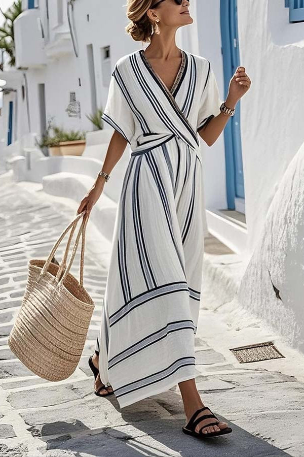Woman in a white and blue striped dress holding a straw bag on a sunlit street.