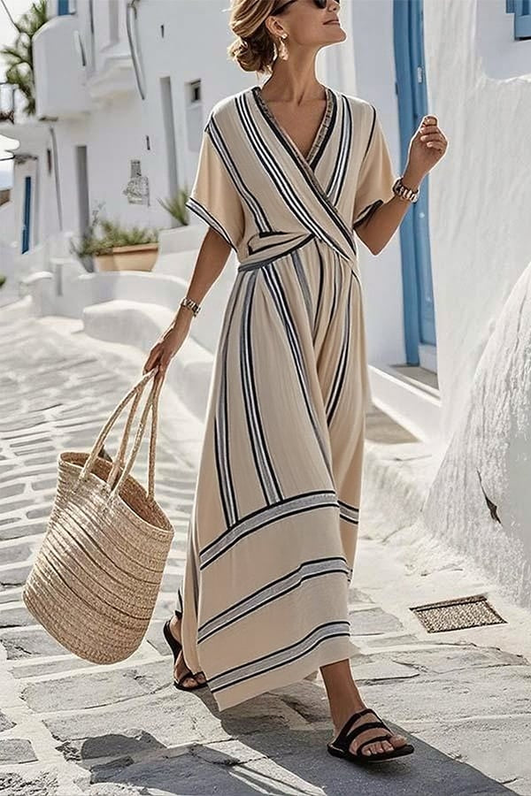 Woman in a striped dress walking on a sunlit street with white buildings.