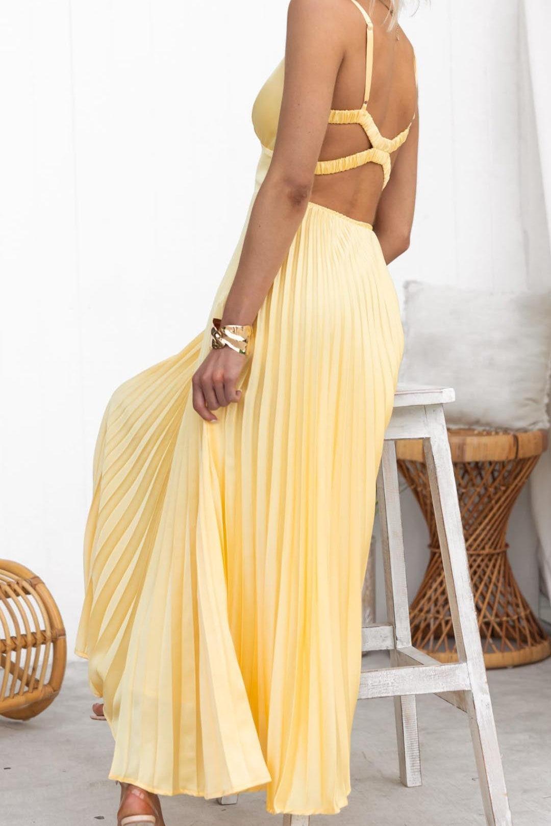 Woman wearing a yellow dress standing next to a white stool with wicker accents.