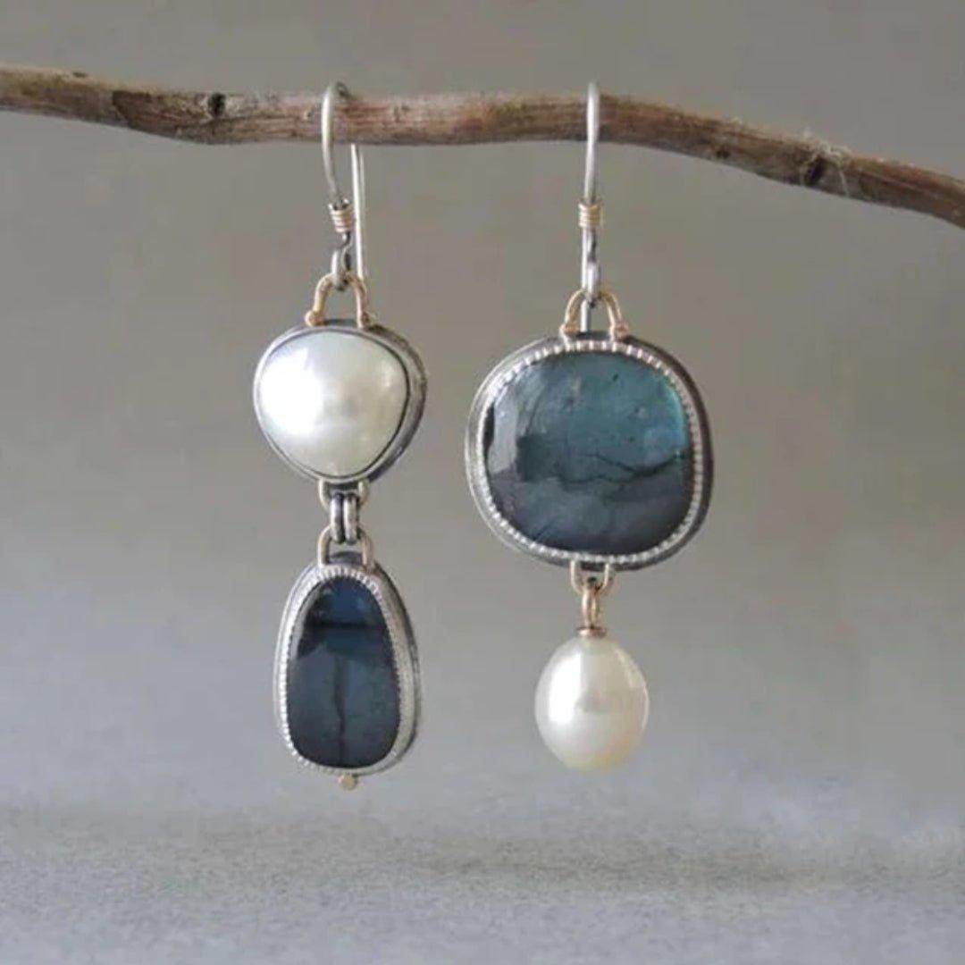 Pair of earrings with blue and white stones hanging on a branch.