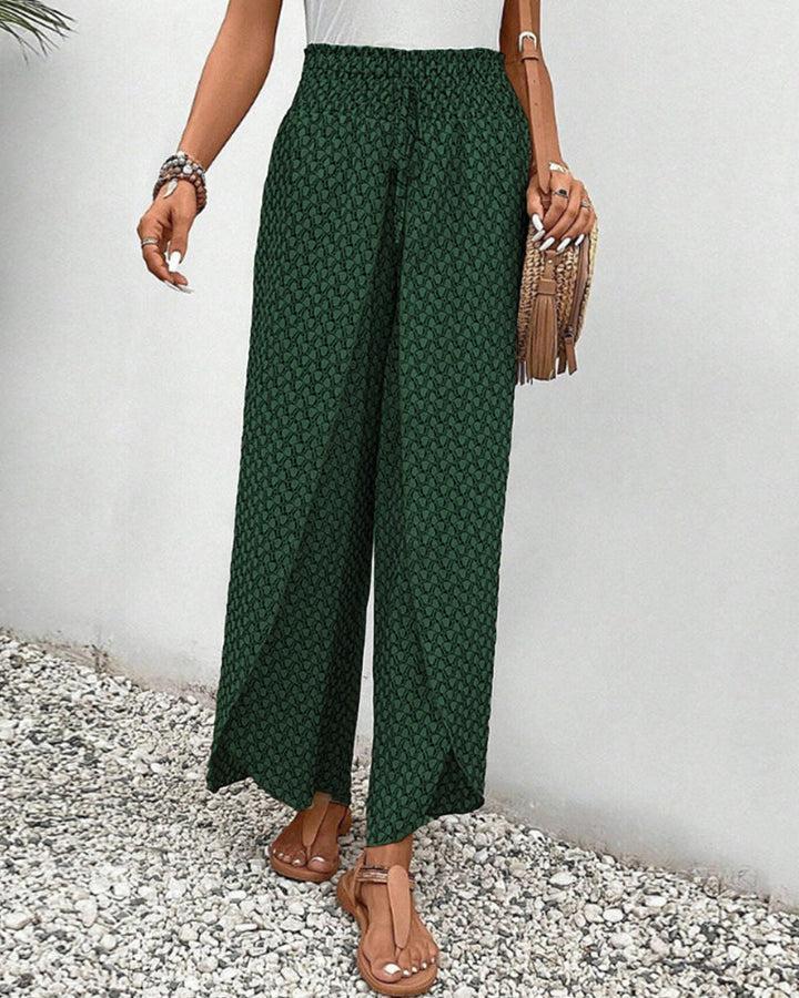 Person wearing green patterned pants with a white top and brown sandals on a gravel surface.