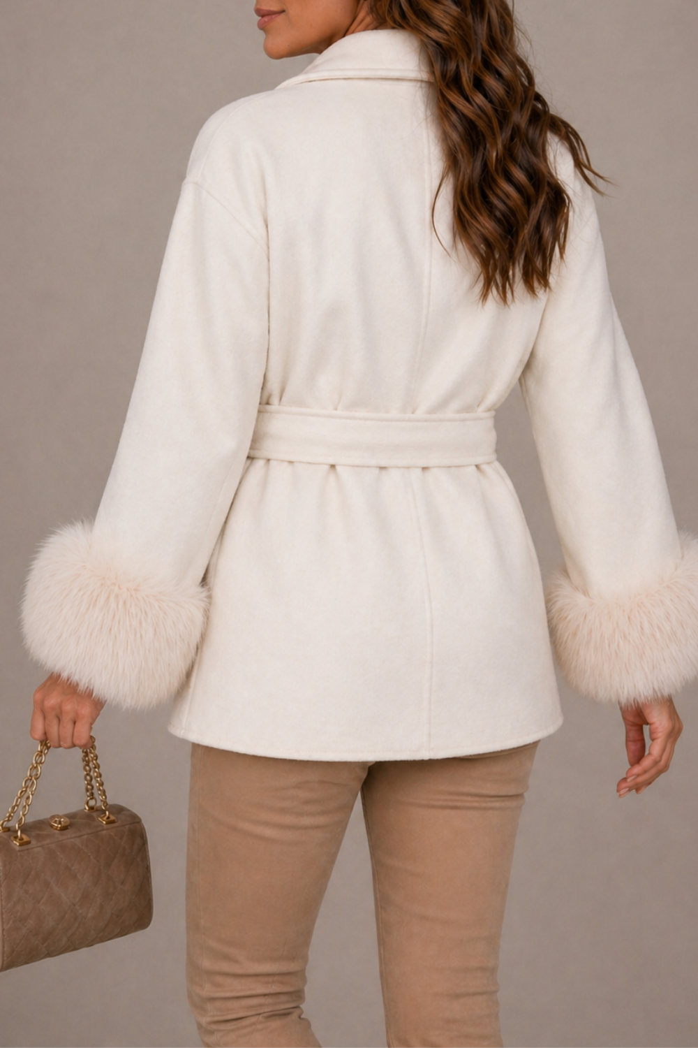 Woman wearing a white coat with fur trim holding a brown handbag against a neutral background