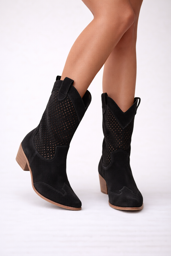 Black cowboy boots worn by a person on a white background