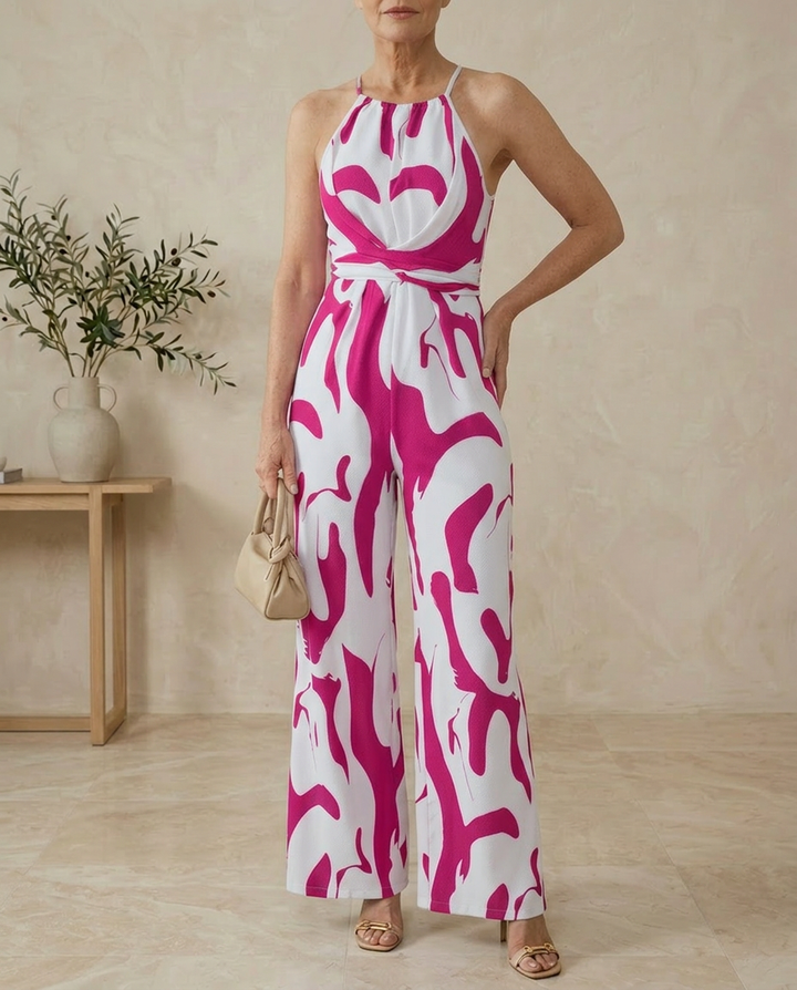 Woman wearing a pink and white patterned jumpsuit in a room with a wooden table and vase.