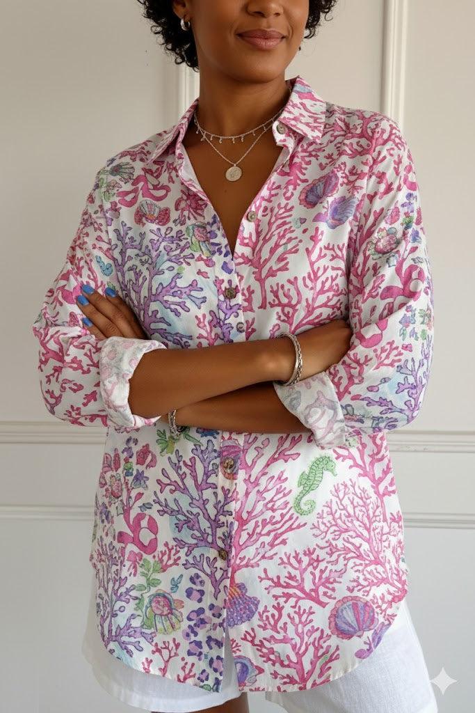 Woman wearing a colorful floral shirt with her arms crossed against a white wall.
