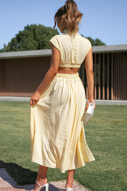 Woman in a yellow dress standing on grass with a building in the background