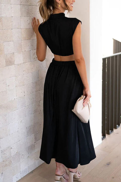 Woman in a black dress standing against a light stone wall.