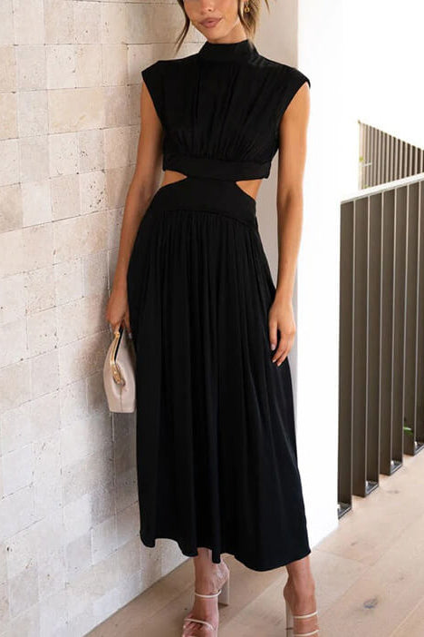 Woman wearing a black dress with cut-out design against a light stone wall.
